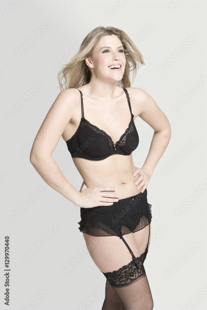Naklejka premium Cheerful beautiful woman in sexy black underwear against gray background
