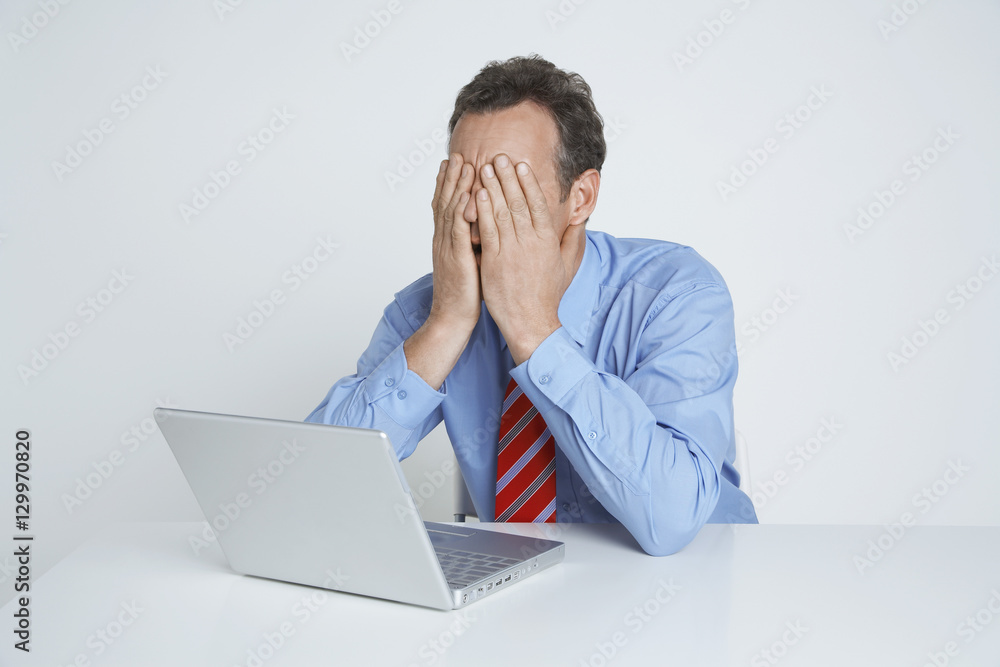 Depressed businessman with laptop at desk isolated over white background Depressed businessman with laptop at desk isolated over white background