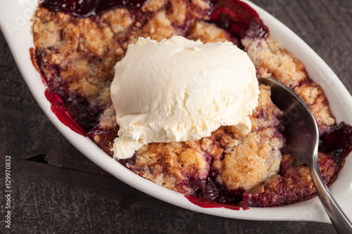 Slika na platnu Close up of small white aramekian bowl of boysenberry cobbler on dark wood backg