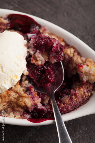 Macro shot of small white aramekian bowl of boysenberry cobbler on dark wood background photo