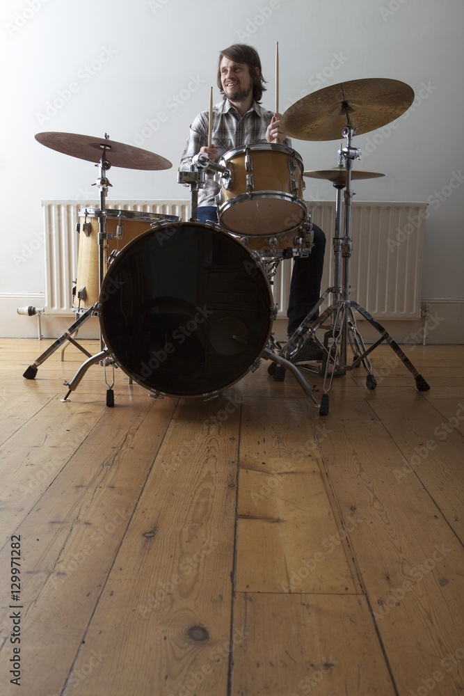 Fototapeta premium Full length of a smiling young man playing drum set on wooden floor