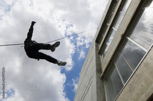 Fotografie Low angle view of SWAT team officer rappelling from building against cloudy sky