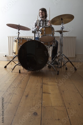 Full length of a smiling young man playing drum set on wooden floor photo