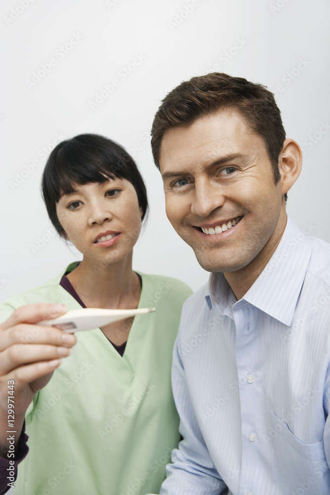 Portrait of happy patient with female doctor looking at thermometer in the clinic Portrait of happy patient with female doctor looking at thermometer in the clinic