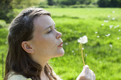 Closeup side view of a woman blowing dandelion seeds