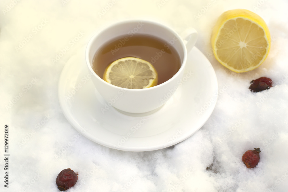 white mug of tea on a saucer with a lemon and wild rose on snow white mug of tea on a saucer with a lemon and wild rose on snow