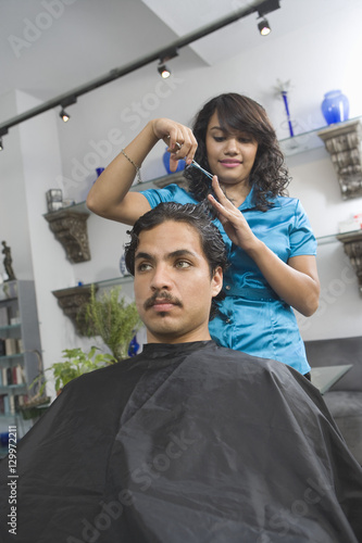 Young female hairdresser cutting man's hair at salon