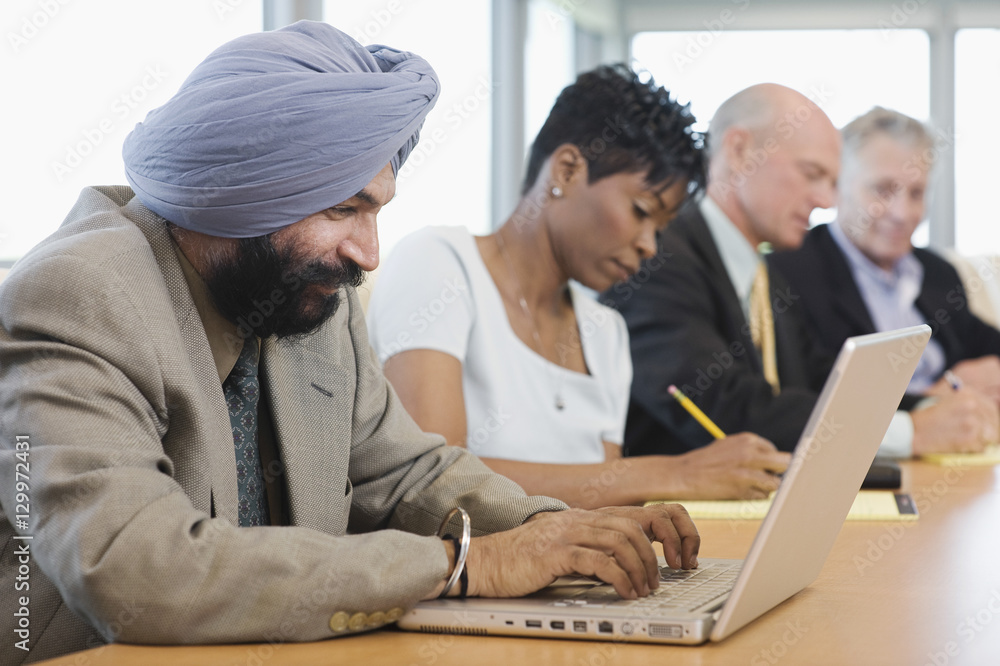 Side view of a businessman using laptop besides multiethnic colleagues in conference room Side view of a businessman using laptop besides multiethnic colleagues in conference room