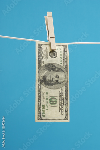 American hundred dollar bill pinned on a clothesline over blue background photo