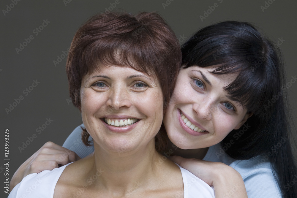 Closeup of a smiling young woman with her mother against gray background Closeup of a smiling young woman with her mother against gray background