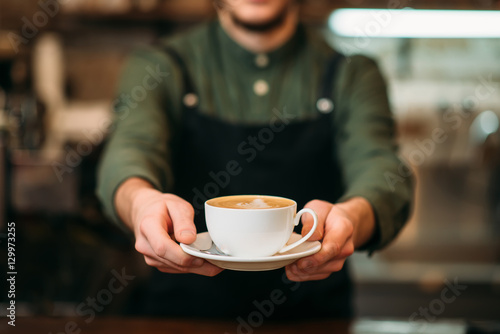 Fotografiet Waiter in black apron stretches a cup of coffee