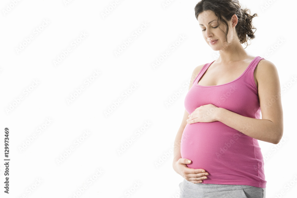 Beautiful young pregnant woman standing with eyes closed against white background Beautiful young pregnant woman standing with eyes closed against white background