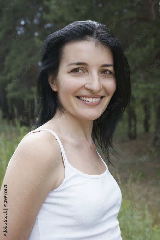 Portrait of a smiling woman in tank top against blurred plants Portrait of a smiling woman in tank top against blurred plants