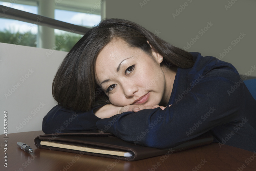Closeup portrait of a bored Asian businesswoman with head on desk Closeup portrait of a bored Asian businesswoman with head on desk