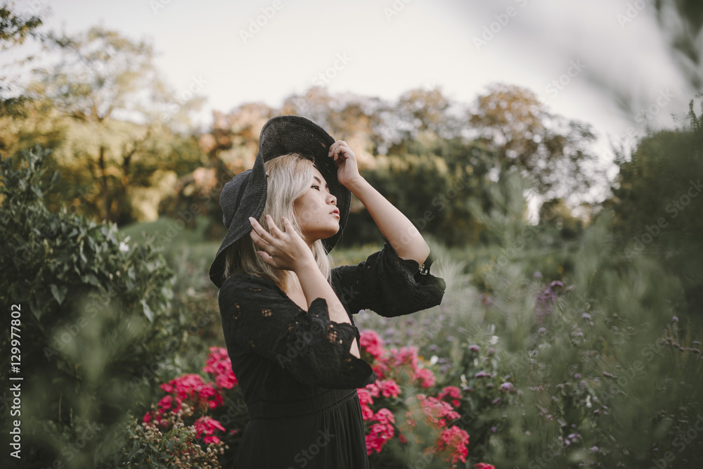 Young asian Woman wearing a fashionable hat and black dress surrounded by flowers Young asian Woman wearing a fashionable hat and black dress surrounded by flowers