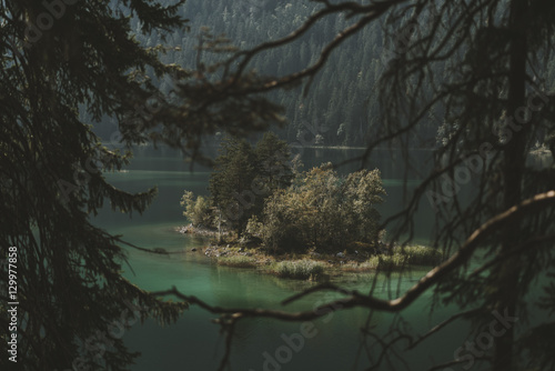 Island with wild trees in a lake surrounded by a mountain forest and framed by branches