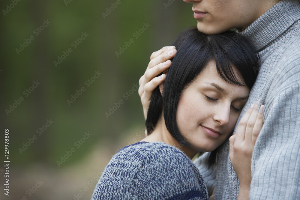Closeup side view of a young woman laying head on man's chest against blurred background