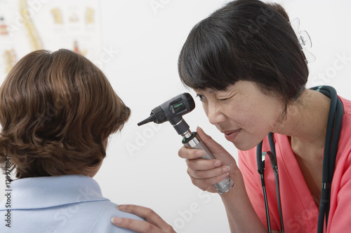 Female doctor checking preadolescent patient ear with otoscope in the clinic