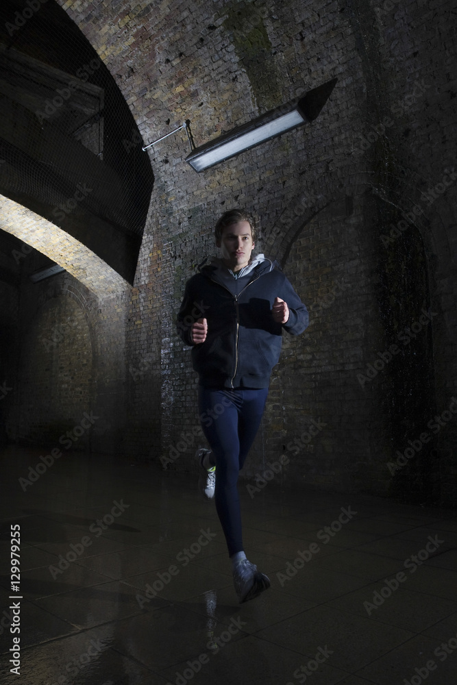 Full length of a young man jogging through urban tunnel at night Full length of a young man jogging through urban tunnel at night