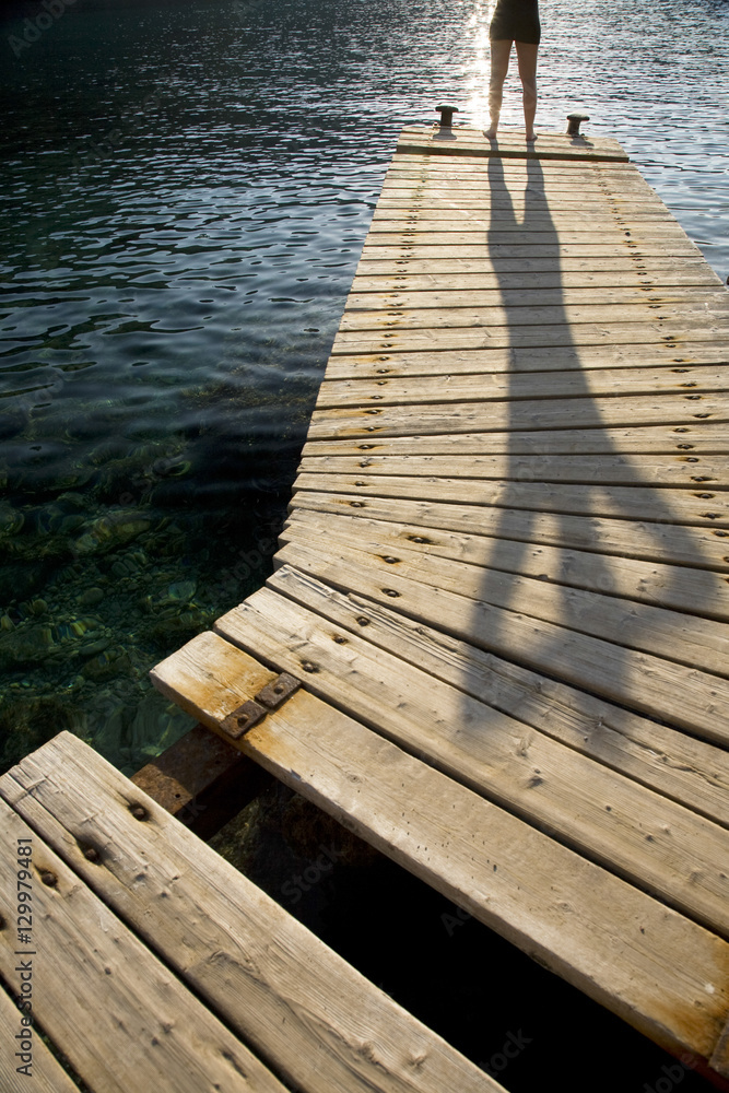 Obraz premium Distance shot of a person standing on wooden jetty by peaceful lake