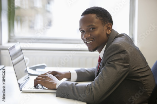Portrait of happy African American businessman using laptop at office desk © moodboard
