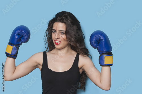 Portrait of a beautiful young female boxer raising arms in victory against blue background