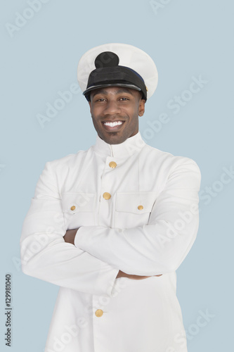Portrait of a happy young US Navy officer standing with arms crossed over light blue background