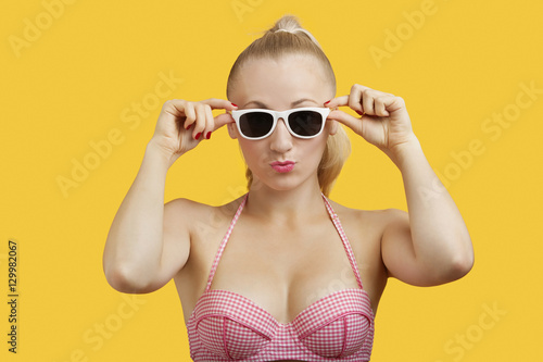 Portrait of a beautiful young woman in sunglasses puckering lips over yellow background