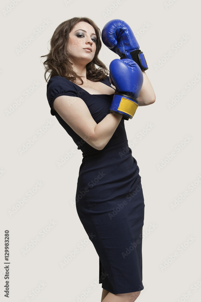 Portrait of a young woman wearing blue boxing gloves against gray background Portrait of a young woman wearing blue boxing gloves against gray background