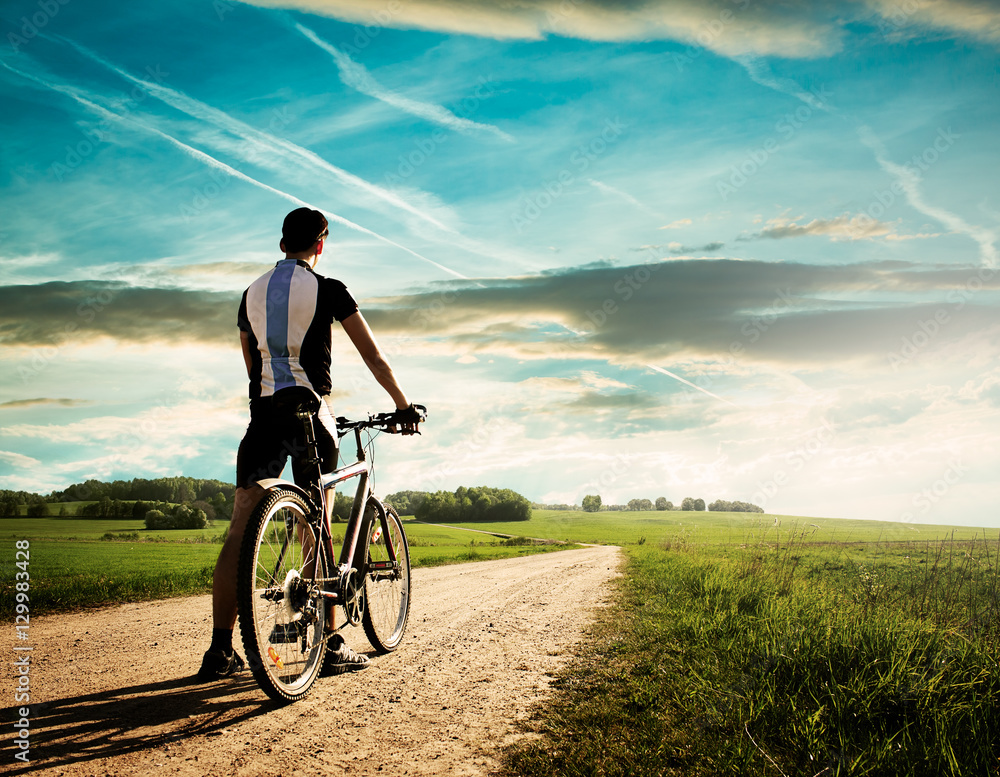 Rear View of a Young Man With Bicycle on Summer Nature Background. Healthy Lifestyle and Mountain Bike Cycling Concept. Toned Photo with Copy Space. Stock Photo Adobe Stock