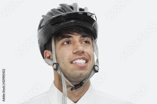 Close-up of Indian businessman wearing cycling helmet while looking away against gray background