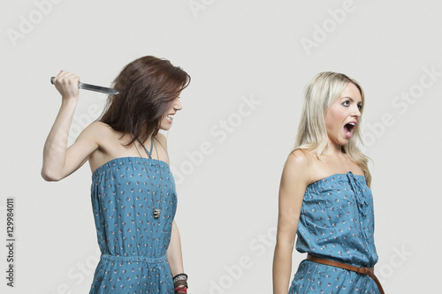 Friend stabbing young woman in similar jump suits from behind
