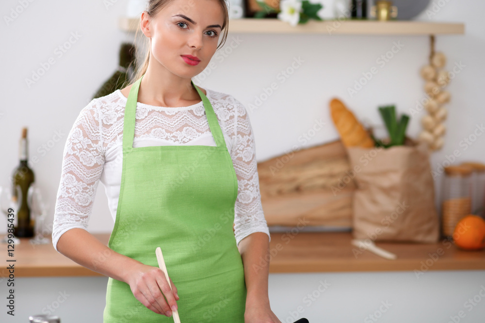 Young woman in the green apron is cooking in the kitchen. Housewife fry the meat in a pan Young woman in the green apron is cooking in the kitchen. Housewife fry the meat in a pan