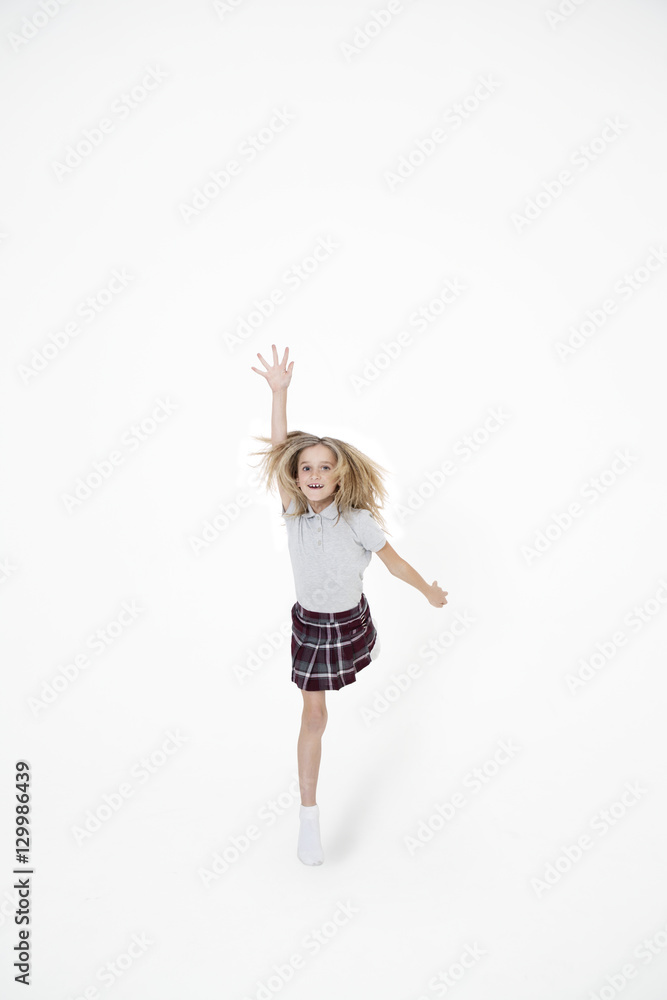 Portrait of school girl jumping with hand raised over white background