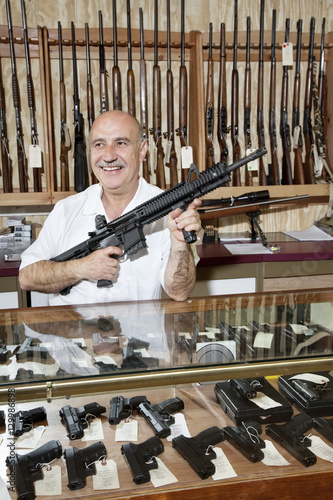 Happy mature man with rifle in gun store