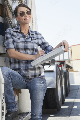 Beautiful woman writing on clipboard while standing by a flatbed truck