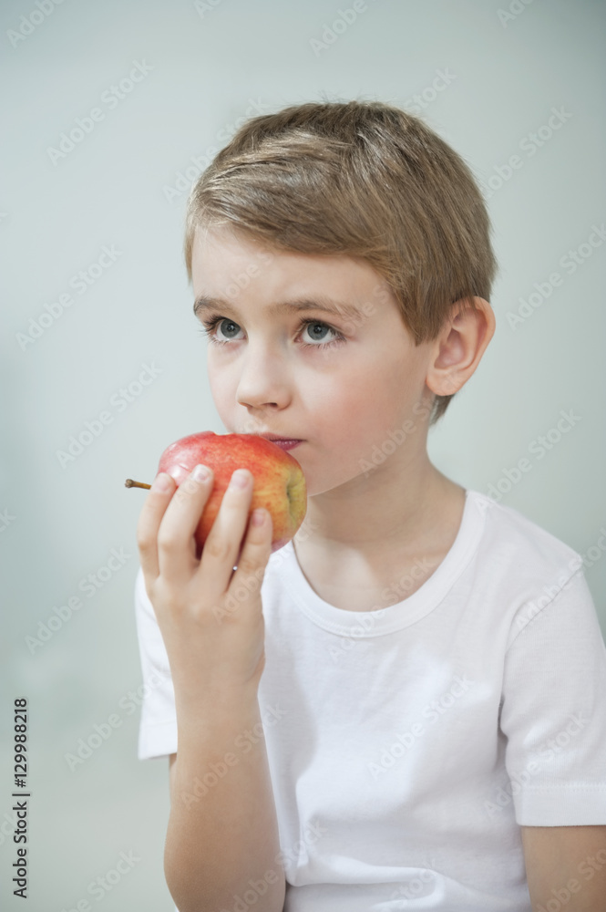 Portrait of young boy eating an apple over gray background Portrait of young boy eating an apple over gray background