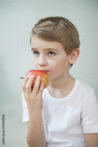 Portrait of young boy eating an apple over gray background