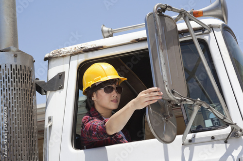 Asian female industrial worker adjusting mirror while sitting in logging truck