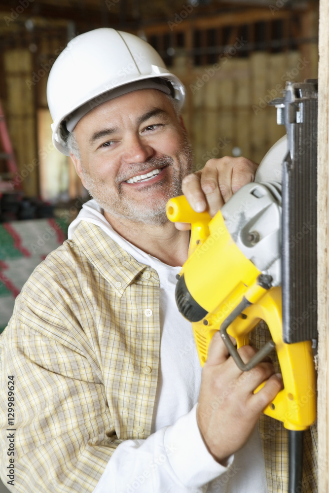 Happy mature male construction worker cutting wood with a circular saw Happy mature male construction worker cutting wood with a circular saw