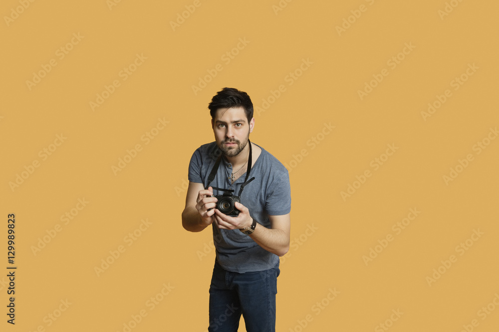 Portrait of a confident young man with camera over colored background Portrait of a confident young man with camera over colored background