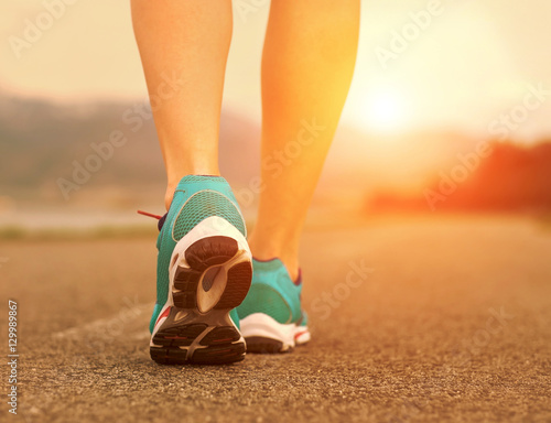 Runner athlete feet running on road under sunlight.