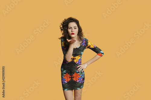 Portrait of a young woman blowing kisses over colored background