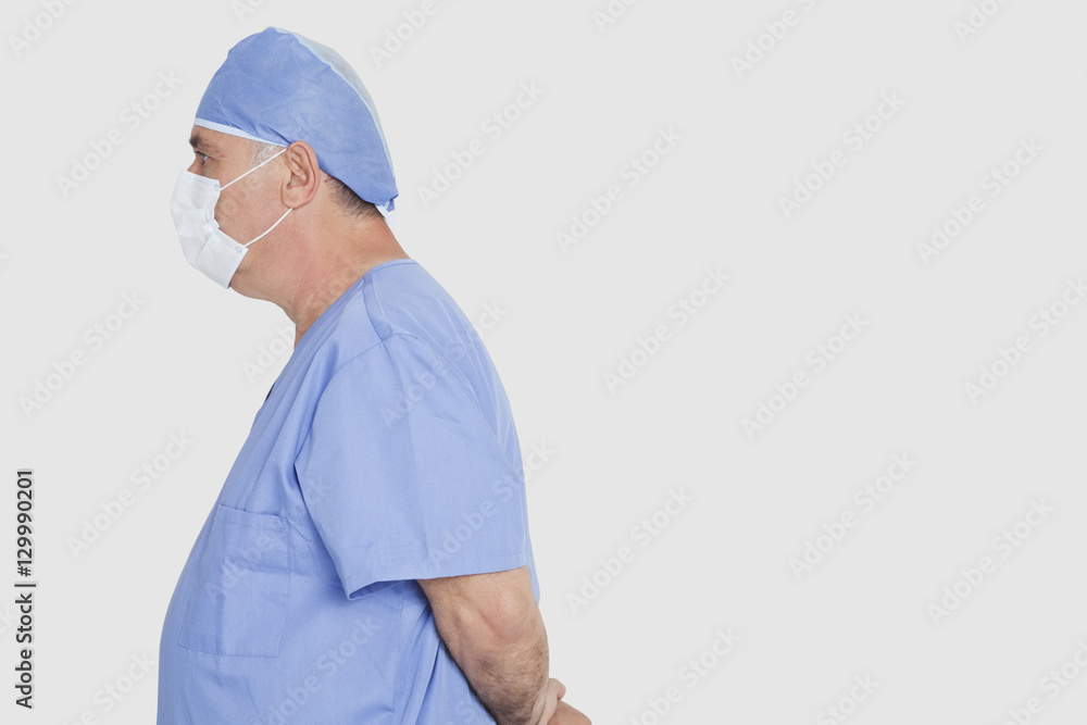 Profile shot of senior male surgeon standing with hands behind back over gray background Profile shot of senior male surgeon standing with hands behind back over gray background