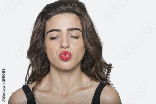Beautiful woman puckering lips with eyes closed over gray background