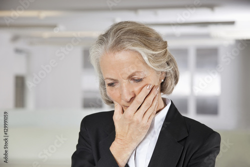 Worried senior businesswoman with hand on mouth in office