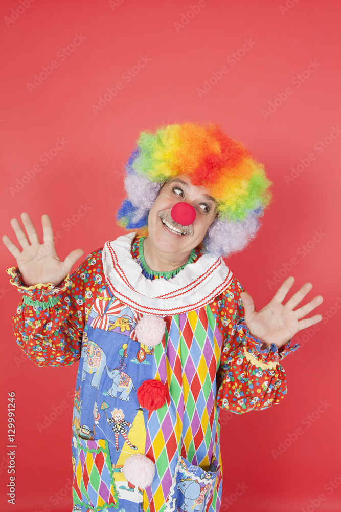 Funny clown with arms raised looking away against colored background Funny clown with arms raised looking away against colored background