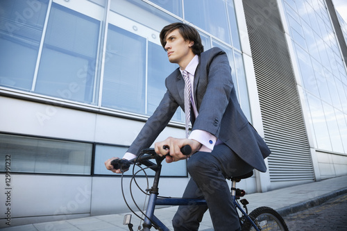 Low angle view of young businessman riding bicycle by building