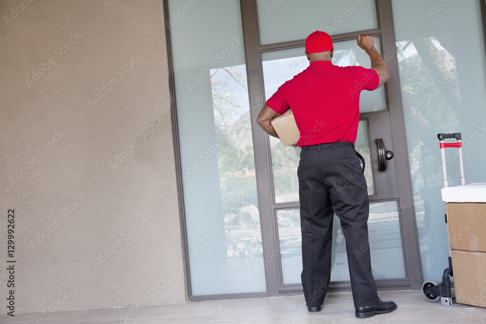 Fototapeta premium Rear view of a delivery man with packages knocking at door