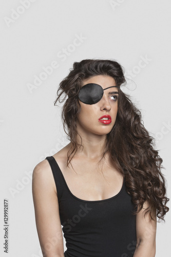 Thoughtful young woman wearing eye patch over gray background